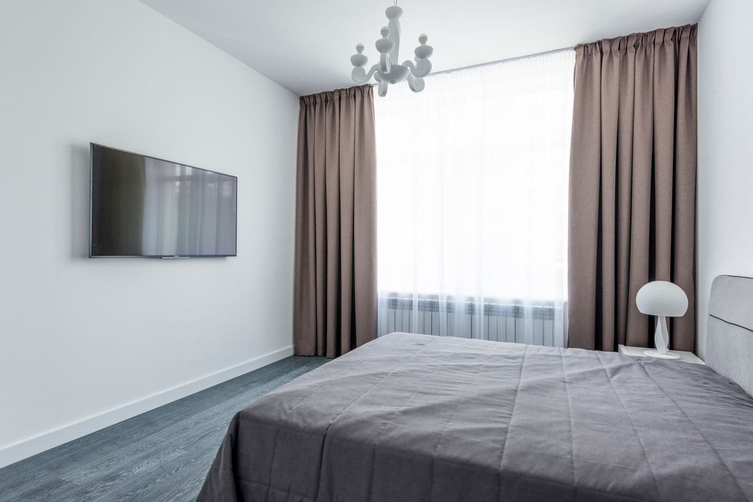 Taupe pencil-pleat drapes layered over a white sheer in a bright bedroom