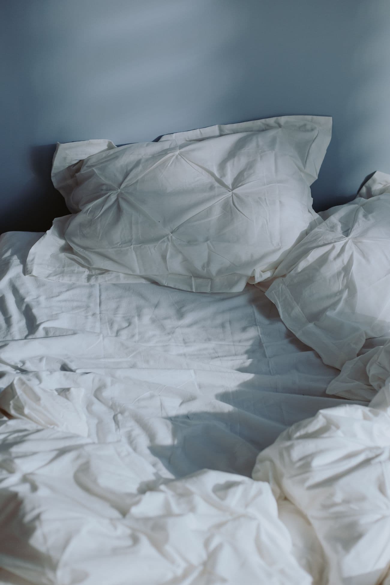 Soft white pillows and bedding against a soft blue-grey wall
