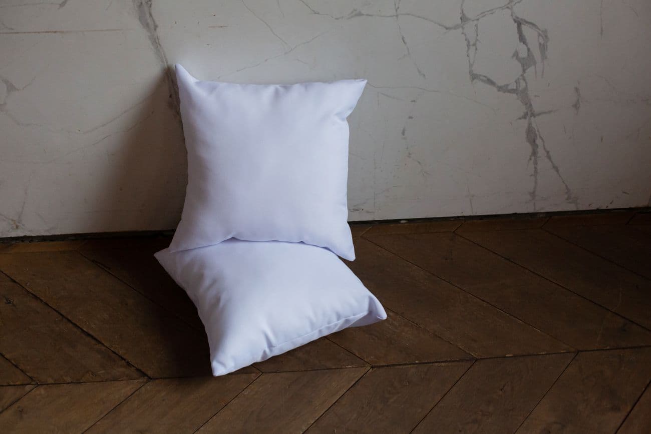A pair of soft white scatter pillows stacked on a wood floor