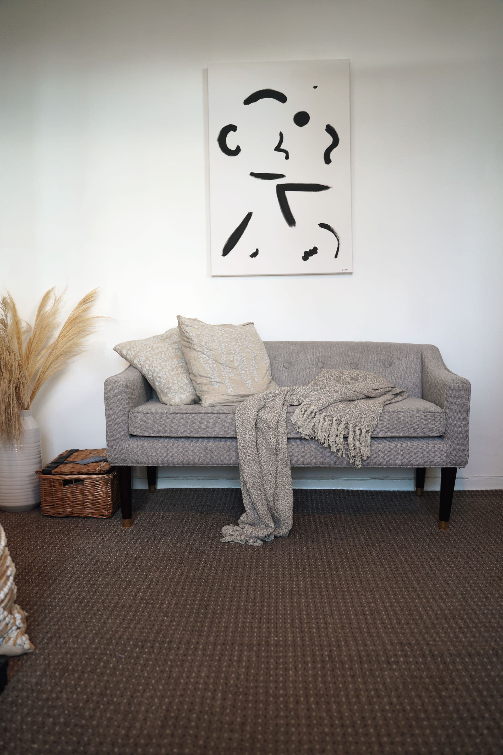 A soft grey sofa styled with cream cushions and a draped fringed throw