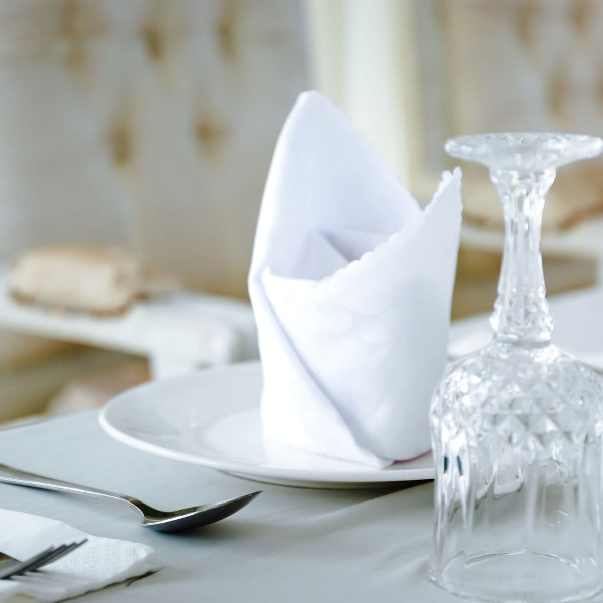 A crisp white napkin folded beside a crystal glass on a white plate